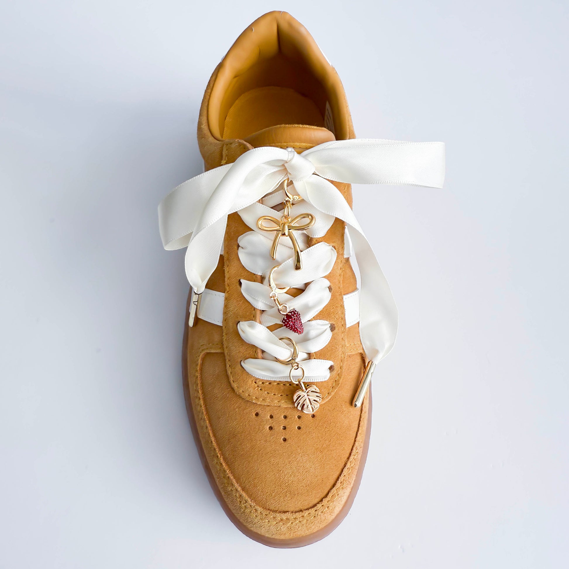 Tan shoe with white laces and decorative charms on a light gray background
