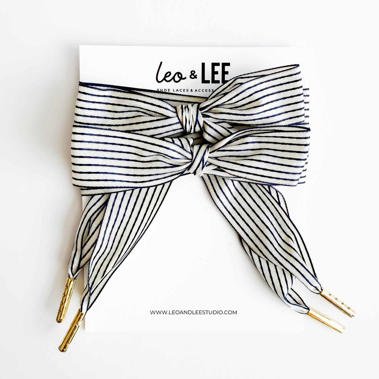 Black and white striped shoelace with gold tips on a white background, branded 'Leo & Lee'.