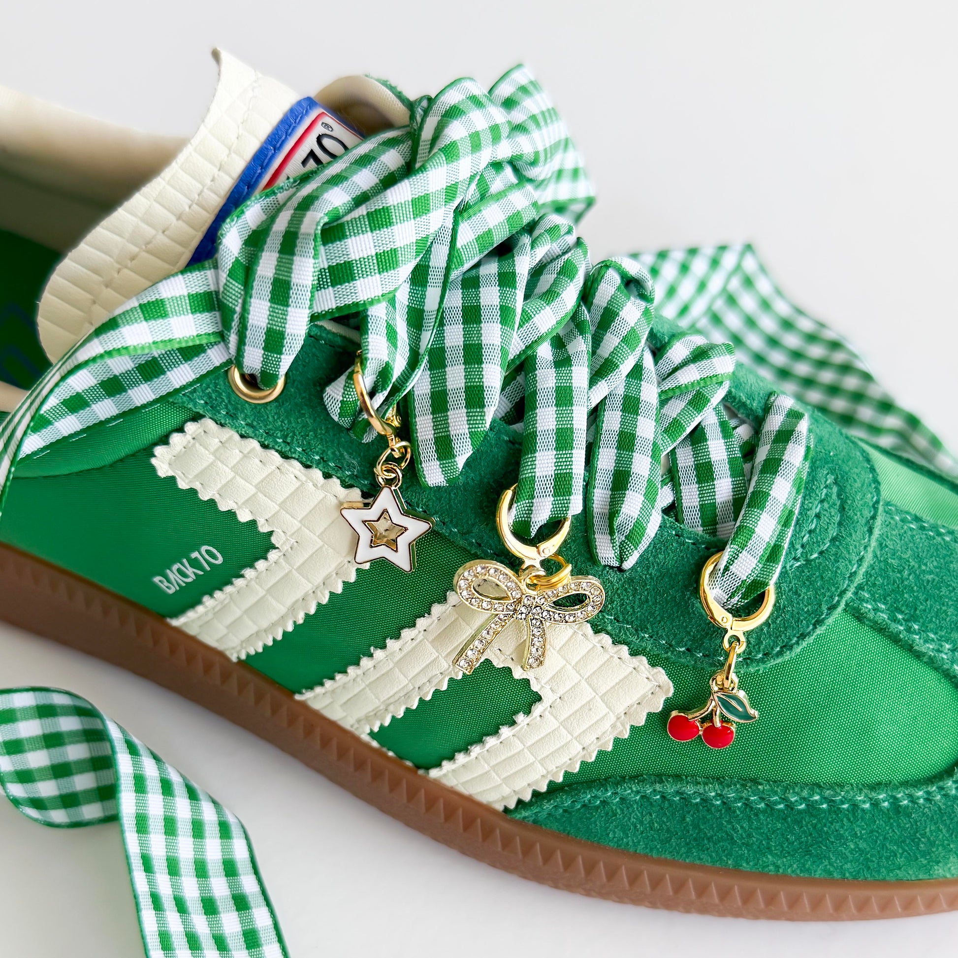 Green gingham bow shoelace accessories with gold sneaker charms – star, cherry, and rhinestone bow – laid out on a Leo and Lee Studio card.