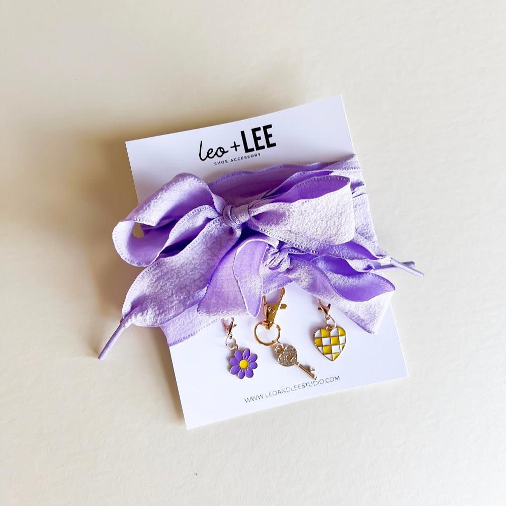 Leo + Lee lavender shoe charms set with purple ribbon laces, featuring a flower, key, and checkered heart charm on a white background.
