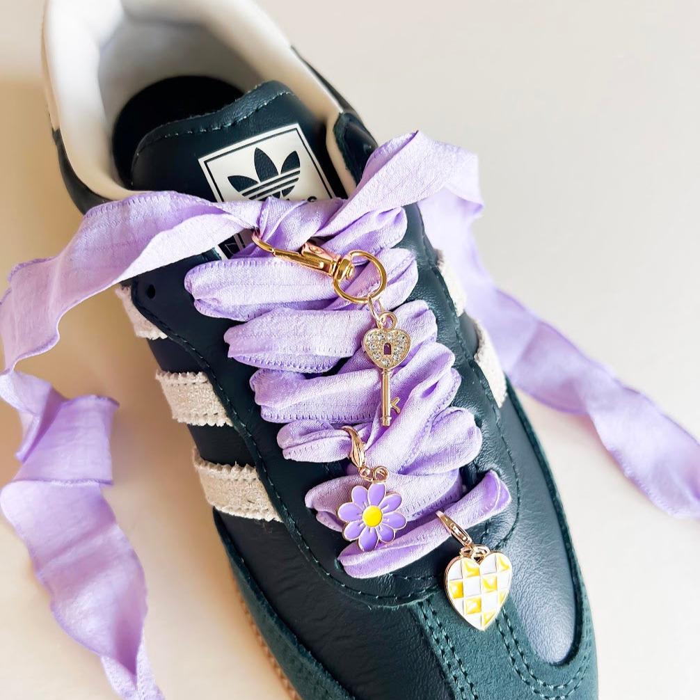Leo + Lee lavender shoe charms set with purple ribbon laces, featuring a flower, key, and checkered heart charm on a white background.