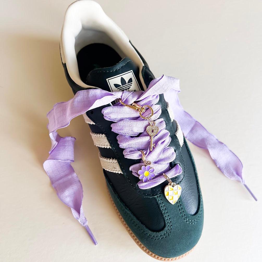 Leo + Lee lavender shoe charms set with purple ribbon laces, featuring a flower, key, and checkered heart charm on a white background.