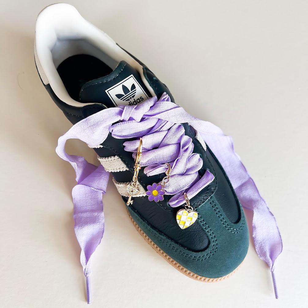 Leo + Lee lavender shoe charms set with purple ribbon laces, featuring a flower, key, and checkered heart charm on a white background.