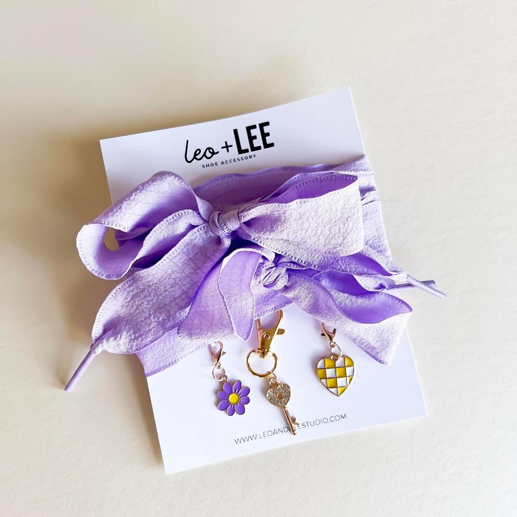 Leo + Lee lavender shoe charms set with purple ribbon laces, featuring a flower, key, and checkered heart charm on a white background.