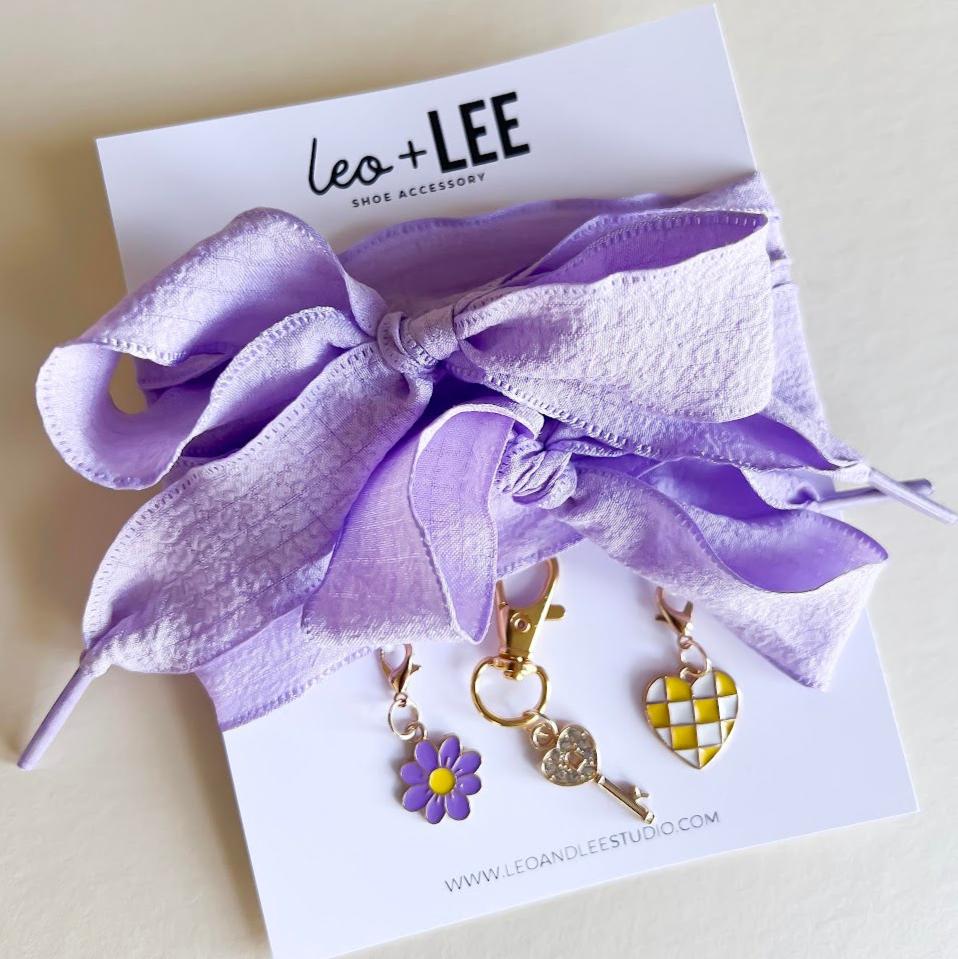 Leo + Lee lavender shoe charms set with purple ribbon laces, featuring a flower, key, and checkered heart charm on a white background.