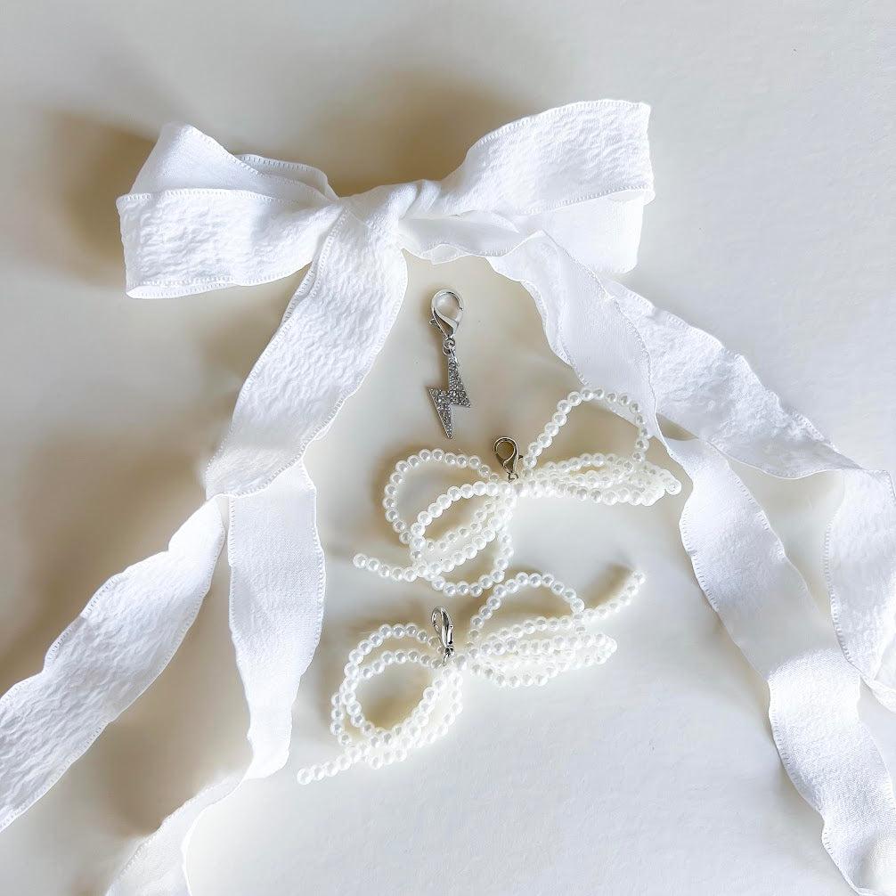 Leo + Lee white pearl and bow shoe charm set with elegant white ribbon laces, featuring a pearl chain and bow charm on a white background.