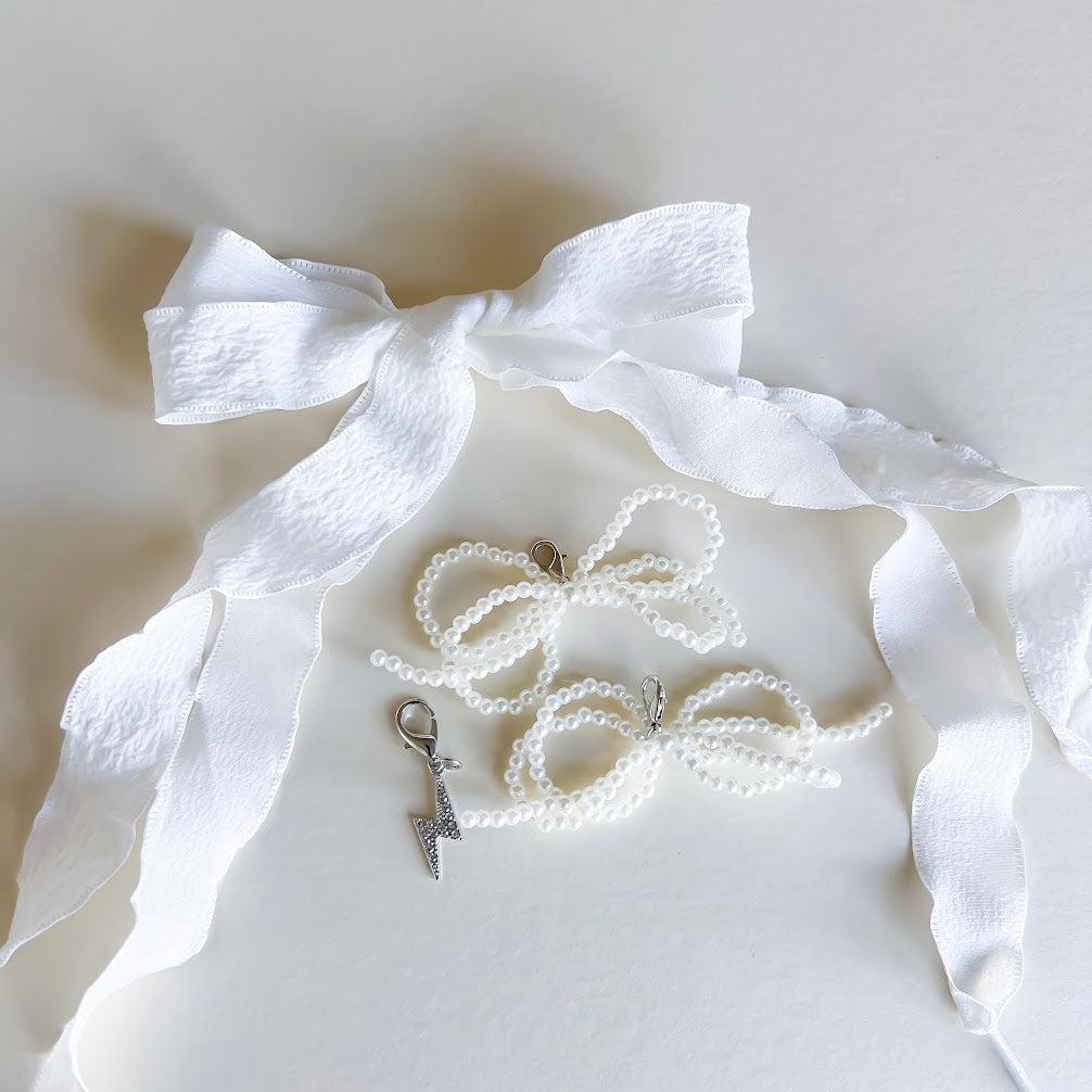 Leo + Lee white pearl and bow shoe charm set with elegant white ribbon laces, featuring a pearl chain and bow charm on a white background.