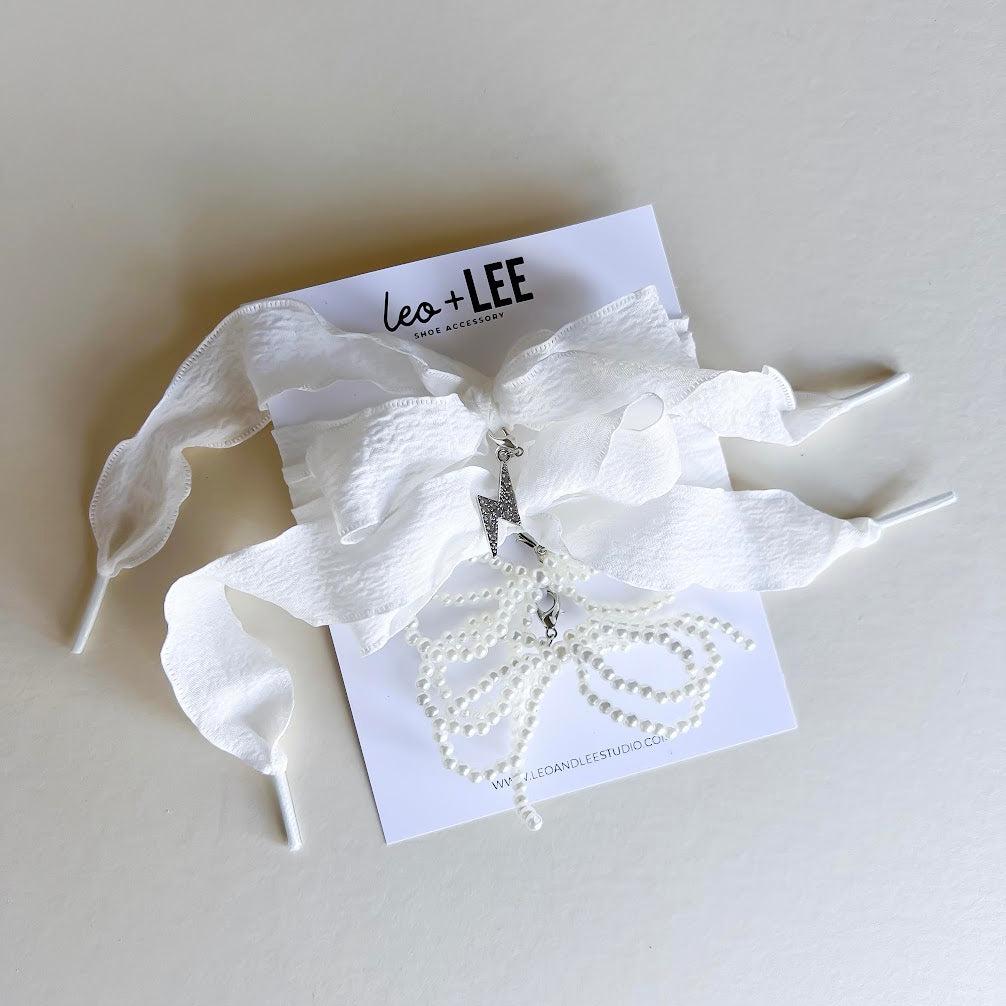 Leo + Lee white pearl and bow shoe charm set with elegant white ribbon laces, featuring a pearl chain and bow charm on a white background.