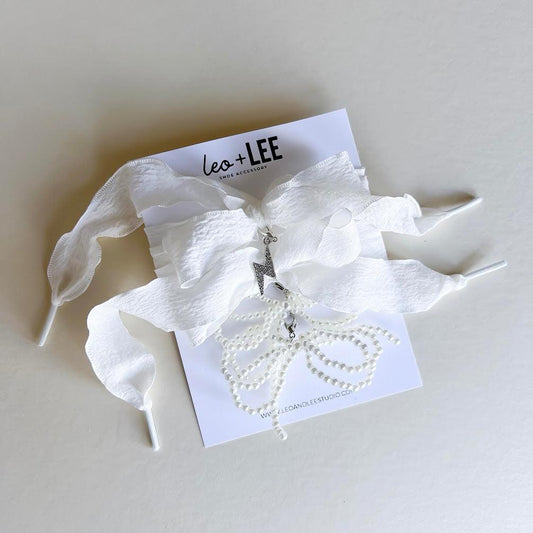 Leo + Lee white pearl and bow shoe charm set with elegant white ribbon laces, featuring a pearl chain and bow charm on a white background.