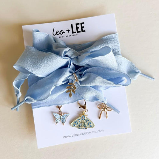 Leo + Lee blue ribbon shoe charm set featuring butterfly, moth, leaf, and bow charms displayed on a white background.