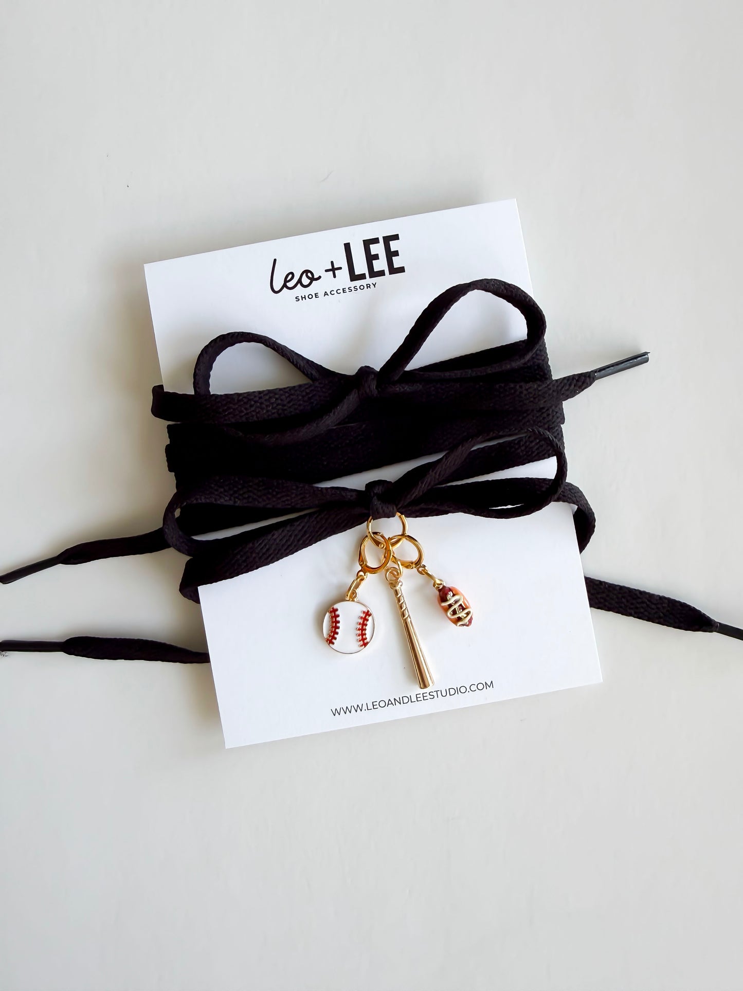 Black flat laces with sports-themed charms on a white card with 'Leo + Lee' branding.